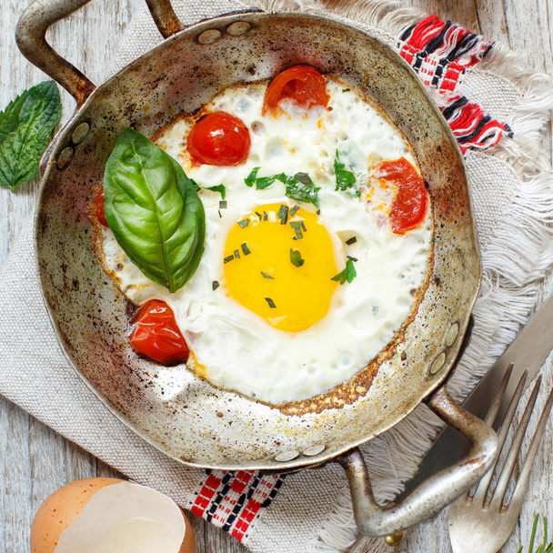 Sahanda yumurta domates ve otlar üzerinde eski bir kızartma tavası - Fotoğraf, Görsel