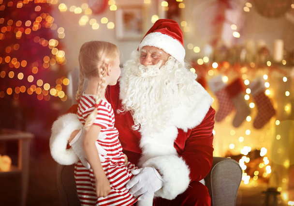 Cute little girl sitting on Santa's lap in room with beautiful Christmas decorations - 写真・画像