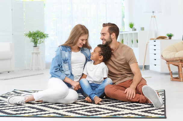 Happy couple with adopted African-American boy sitting on carpet at home - Fotografie, Obrázek