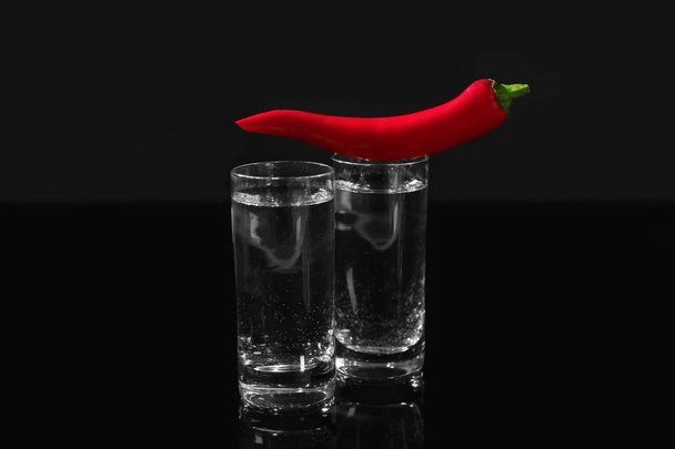 Two glasses with drinks and red chili pepper on black background - Foto, Imagen