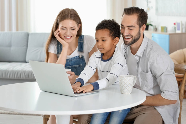 Happy couple with adopted African-American boy using laptop in living room - Foto, immagini
