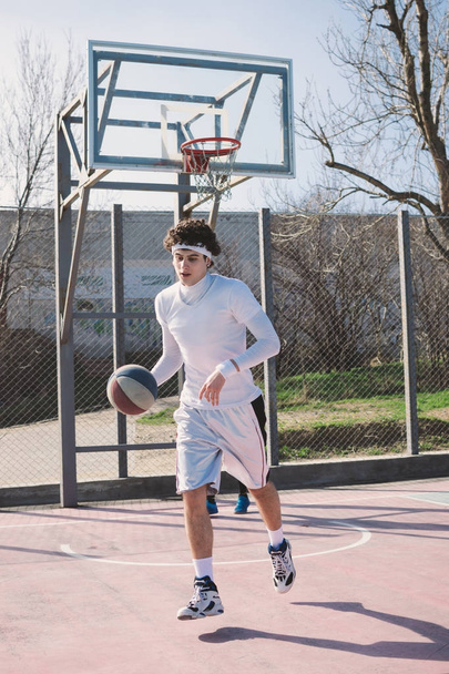 Portrait of a basketball player walking on an outdoor basketball court and dribbling the ball - Foto, Bild