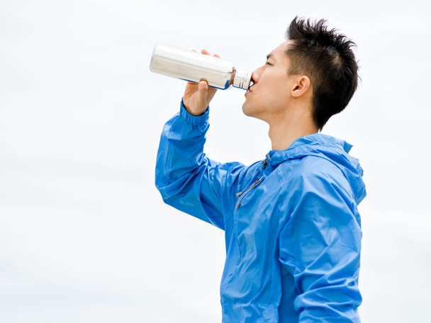 Young man in sport clothes drinking water after workout on the beach - Foto, Imagen
