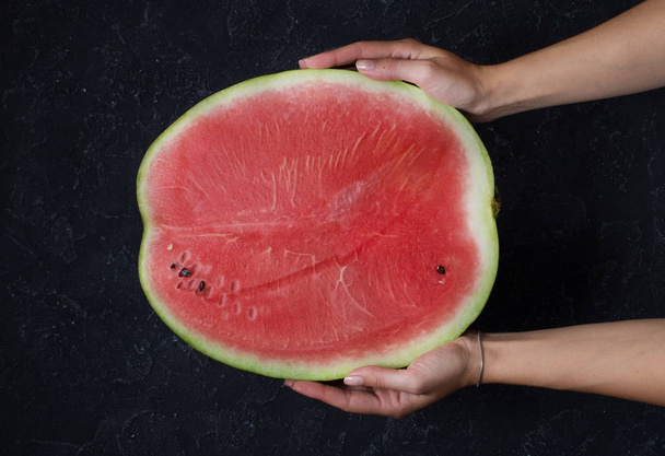 Half of watermelon holding by hand on dark background - Фото, изображение