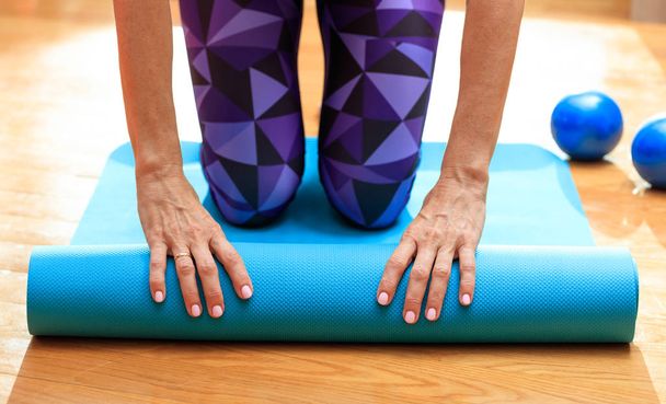 Frau rollt Yogamatte auf Holzboden - Foto, Bild