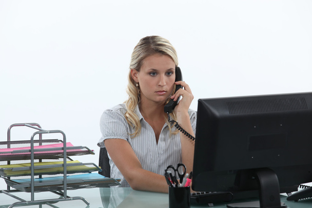 Woman sitting at her desk on the phone - Foto, afbeelding