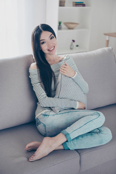 Young charming asian girl is holding grey pillow, sitting on bei - Φωτογραφία, εικόνα