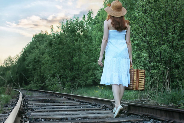 Tyttö valkoinen sundress ja paju matkalaukku kävely kiskoilla
 - Valokuva, kuva
