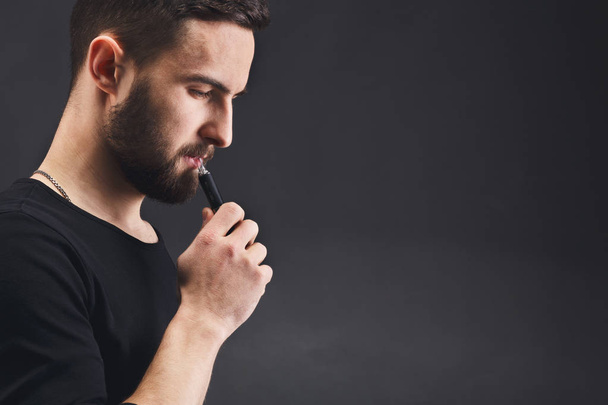 Young man vaping e-cigarette on black - 写真・画像
