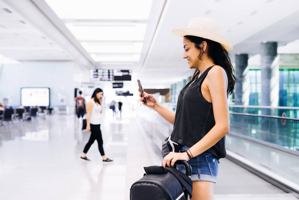 Travel woman using smartphone at airport. Young eastern traveler checking boarding time with mobile phone app - Photo, image