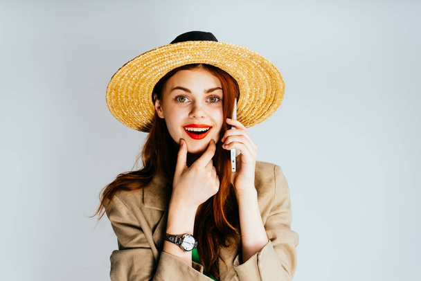 bright red-haired girl with red lips and in a hat talking on the phone and smiling - Fotografie, Obrázek