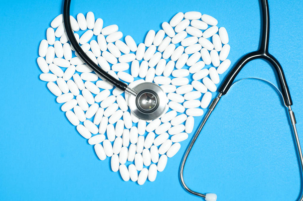 Heart of white pills and stethoscope on blue background - Foto, afbeelding