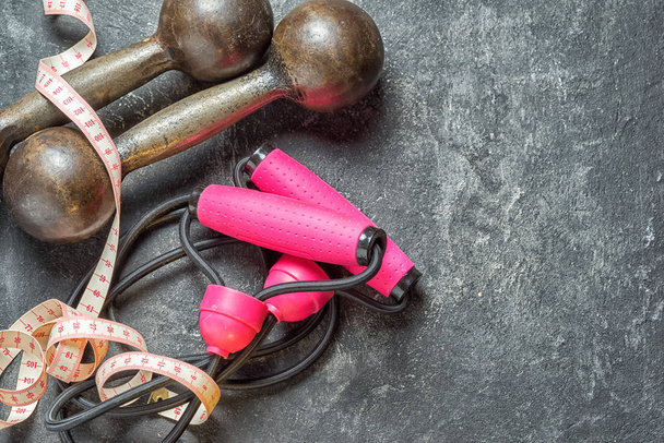Dumbbells, centimeter tape and expander on a dark cement background as a sport conceptual backdrop, top view with copy space for your text. - Photo, Image