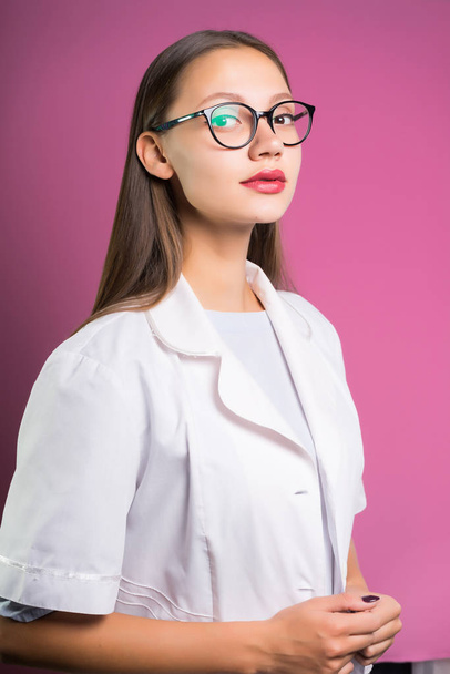 beautiful girl in glasses and a white coat looks into the camera, isolated on a pink background - Foto, Imagem