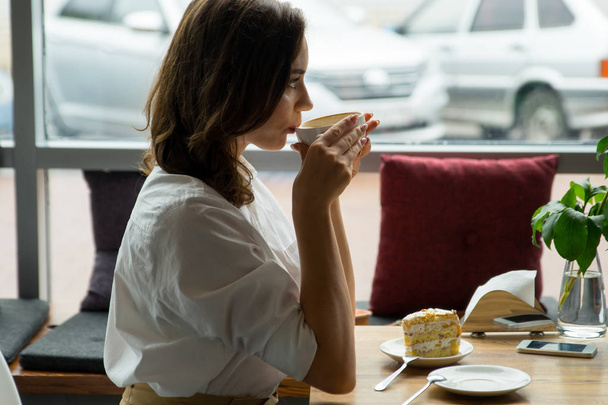 Nuori kaunis nainen, joka juo kahvia kahvilassa. Nuori nainen työvaatteissa lounastauolla
 - Valokuva, kuva