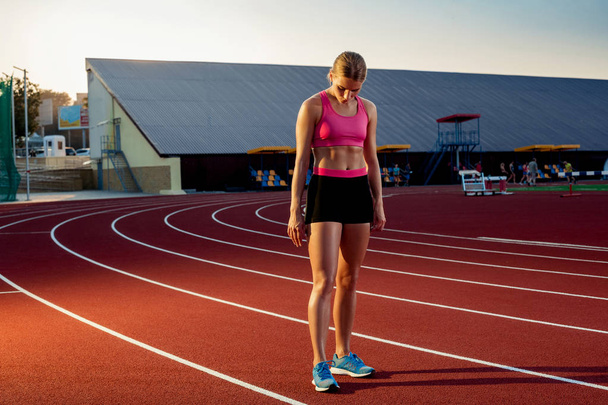 Imagen de la hermosa joven corredora europea o velocista de pie en la pista de estadio al aire libre, sintiéndose agotada después del sprint o maratón
. - Foto, imagen