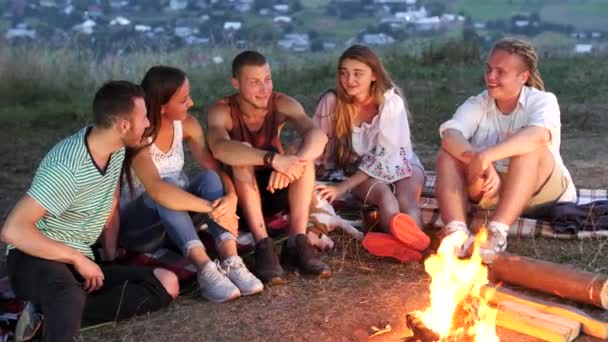 Group of friends sit next to a campfire with warm drinks and talk - Footage, Video