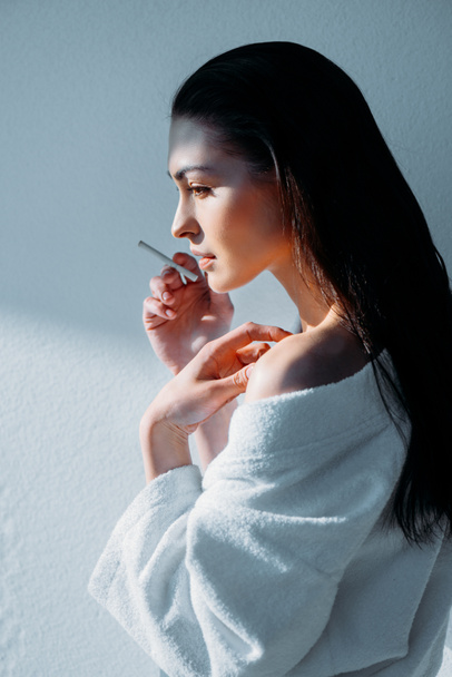 Young woman in bathrobe smoking - Фото, зображення