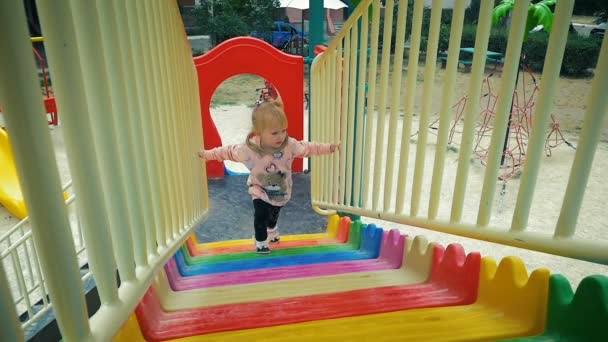 Slow Motion: meisje van drie jaar klimt langzaam op de dia op de speelplaats. - Video