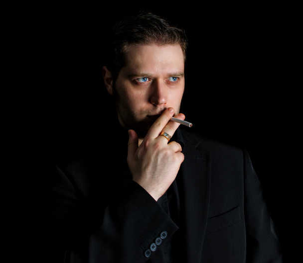 Portrait of smoking man in black suit - 写真・画像