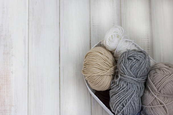 Hilado de lana colores brillantes en una cesta sobre fondo de madera blanca
 - Foto, Imagen