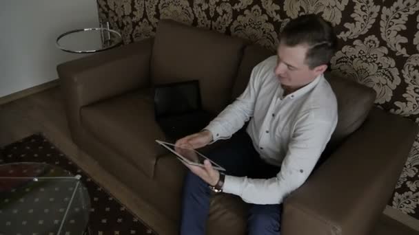 homem de negócios em camisa sentado no sofá e usando tablet digital no quarto
  - Filmagem, Vídeo