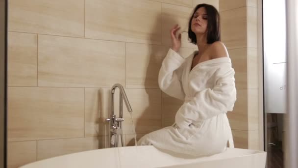 brunette woman in white robe in modern bathroom at home - Кадры, видео