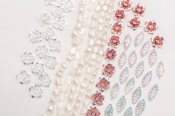 Materiales para el trabajo creativo sobre fondo blanco. Perlas de marfil y plata chapados y encantos de aleación de flor de cobre
 - Foto, imagen