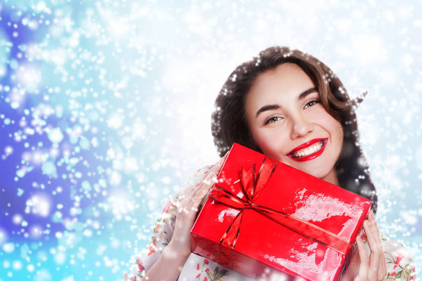 Молода щаслива жінка в барвистій сукні тримає червону подарункову коробку на зимовому тлі, місце для текстових привітань
 - Фото, зображення