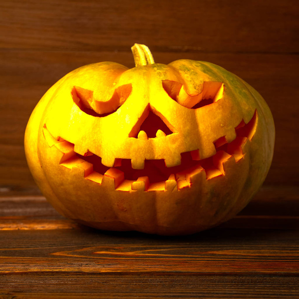 Scary Halloween pumpkin isolated on wooden background . Scary glowing face trick or treat. Concept of halloween pumpkin on wooden planks.  - Fotó, kép