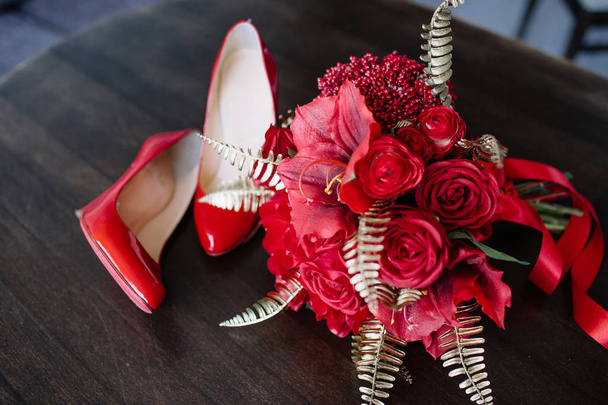 Пара красных туфель на высоких каблуках с букетом на столе
 - Фото, изображение