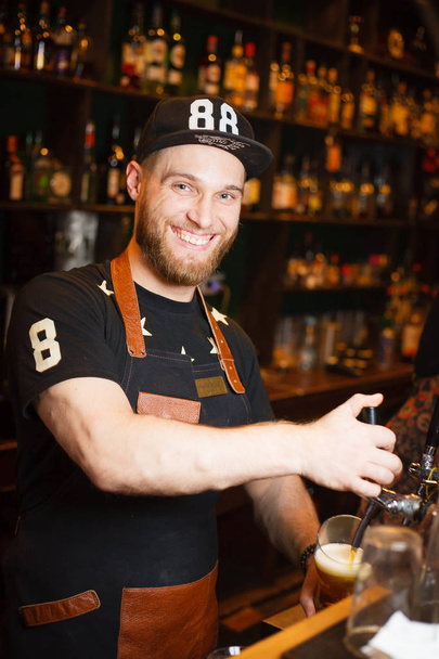 Aangename barman giet bier in de bar - Foto, afbeelding