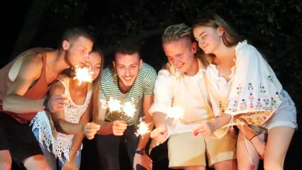 Vrolijke jongeren zittend op het weekend at night met vuurwerk wonderkaarsen. - Video