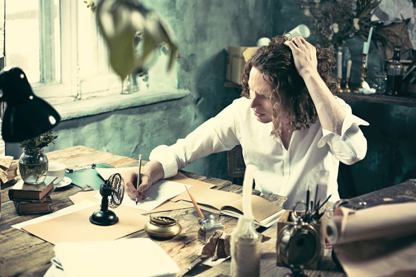 Writer at work. Handsome young writer sitting at the table and writing something in his sketchpad - Фото, зображення