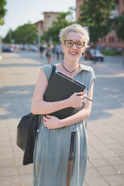 jovem designer loira caucasiano caminhando até a cidade, segurando um caderno de esboços, com vista para a direita - trabalhando, conceito de iluminação
 - Foto, Imagem