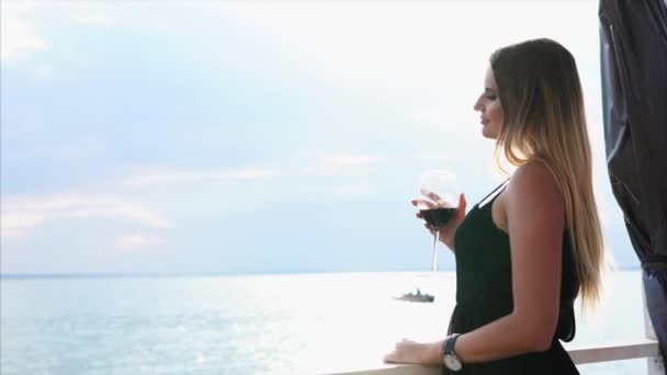 Nuori nainen juo punaviiniä ja katsoo merta, nainen ratsastaa veneellä vedessä
 - Materiaali, video