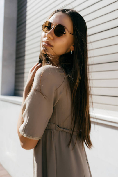 girl in sunglasses stands on the background of wooden blinds - Фото, зображення