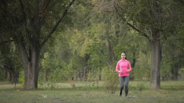 Bastante deportista en ropa deportiva rosa trotando en el bosque, concepto de estilo de vida saludable. Movimiento lento
. - Metraje, vídeo