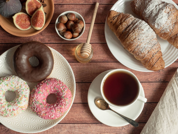 Πρωινό κρουασάν ντόνατ σύκα ξηρούς καρπούς στις πλάκες και τσάι Κύπελλο στο τραπέζι - Φωτογραφία, εικόνα