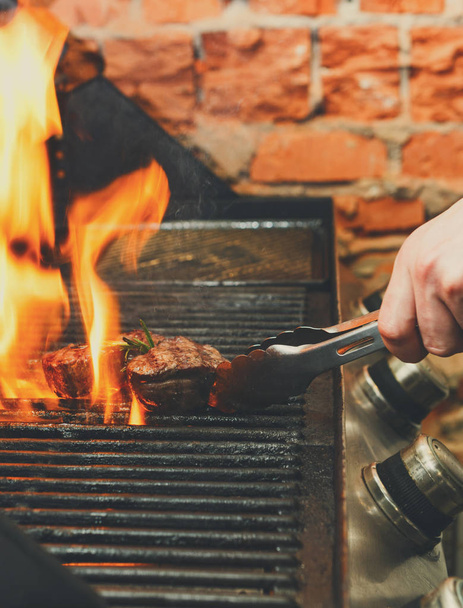 Uomo che cucina bistecche di carne sulla griglia professionale all'aperto
 - Foto, immagini