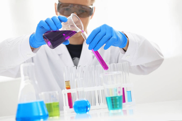 Ένα αρσενικό χημικός κατέχει δοκιμαστικό σωλήνα από γυαλί με το χέρι ξεχειλίζει υγρό διάλυμα - Φωτογραφία, εικόνα