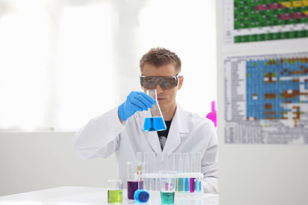 Bir erkek kimyager tüp elinde bardak sıvı bir çözüm taşmaları tutar - Fotoğraf, Görsel