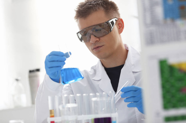Un químico masculino sostiene un tubo de ensayo de vidrio en su mano que desborda una solución líquida
 - Foto, Imagen