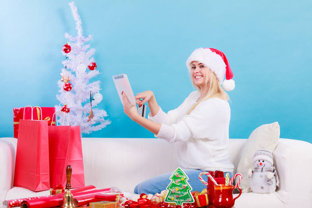 Frau mit Weihnachtsmütze hält Tablet und Kreditkarte in der Hand - Foto, Bild