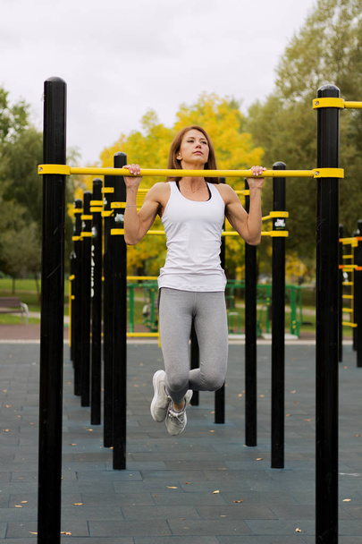 young athletic fitness woman working out at outdoor gym doing pull ups at sunrise. - 写真・画像