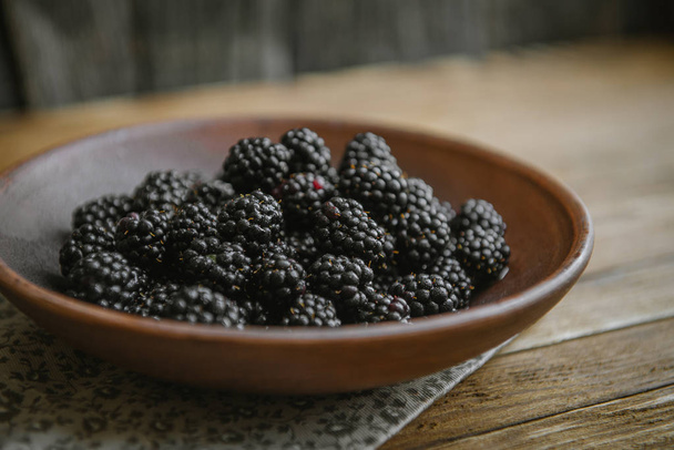 The blackberry in a ceramic bowl lies on a wooden table. - Zdjęcie, obraz