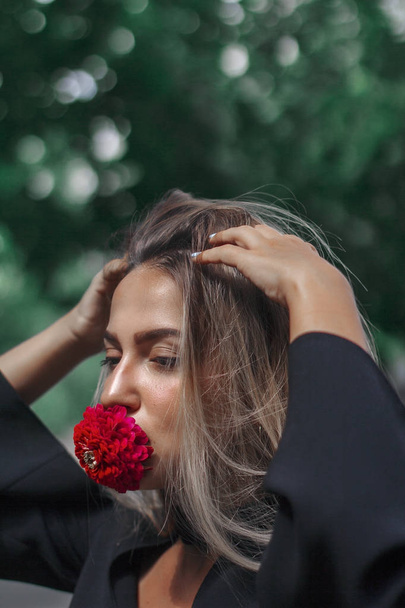 elegante Frau mit einer Blume im Mund. Blütenrot. das Mädchen sieht fantastisch aus. lange schöne Haare. - Foto, Bild