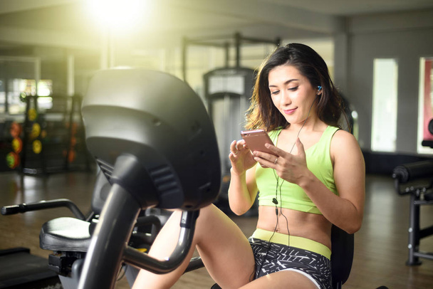 Young sporty woman listening to music on smartphone in gym - Photo, Image