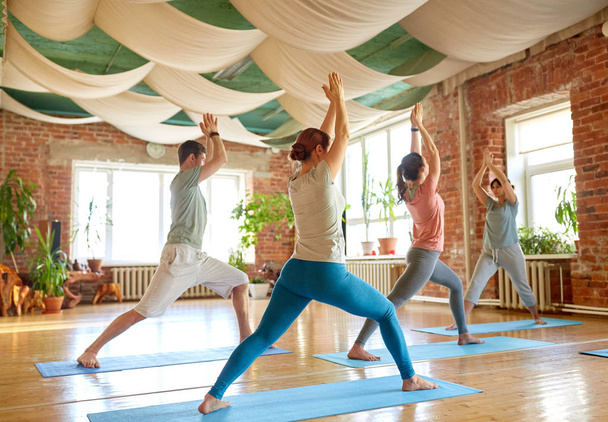 group of people doing yoga warrior pose at studio - Zdjęcie, obraz