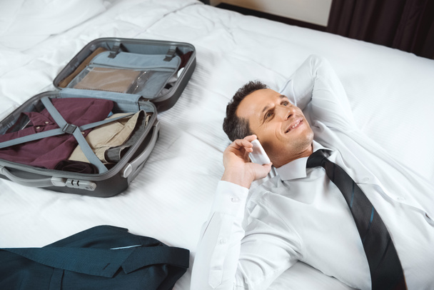 ベッド上で携帯電話で話しているビジネスマン - 写真・画像